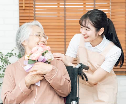 介護士が車椅子の高齢女性に花束を渡している様子